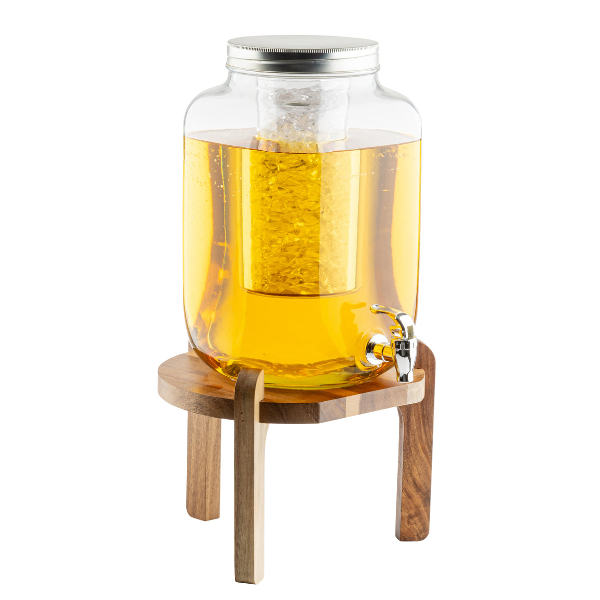 A large TableCraft glass beverage dispenser with a metal lid and silver spigot sits on an acacia wood stand. Filled with yellow-orange liquid, it features an ice core insert to keep drinks cold. The background is plain white.