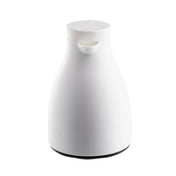 A modern, minimalist white coffee carafe with a glass liner and rounded body features a flat top lid and small spout for pouring. The smooth, handle-free design sits on a dark circular base against a white background.