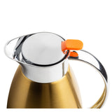 A close-up of a metallic gold TableCraft coffee carafe with a shiny stainless steel lid and handle. The lid features an orange button for opening. The white background makes the carafe's sleek, modern design stand out.
