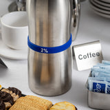 A stainless steel carafe labeled 2% with a blue Silicone Flavor Band stands on a white tablecloth beside a sign reading Coffee, TableCraft Products plates, a cup and saucer, packets of sugar, and an assortment of cookies and pastries.