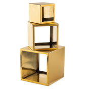 Three metallic gold cubes, resembling a gold riser set, are stacked unevenly. The top cube is solid, while the two below are hollow with open faces. Each is angled differently, forming a modern geometric sculpture.