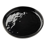 A round, glossy black ceramic serving plate with slightly raised edges sits on a white background. Light reflections highlight its smooth, shiny surface, emphasizing its minimalist and modern design. The plate is empty.