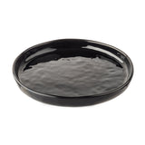 A glossy, round black Serving Plate with slightly raised edges and a subtly textured, wavy surface. Part of the Ridge Collection, this ceramic plate is empty and photographed on a plain white background.