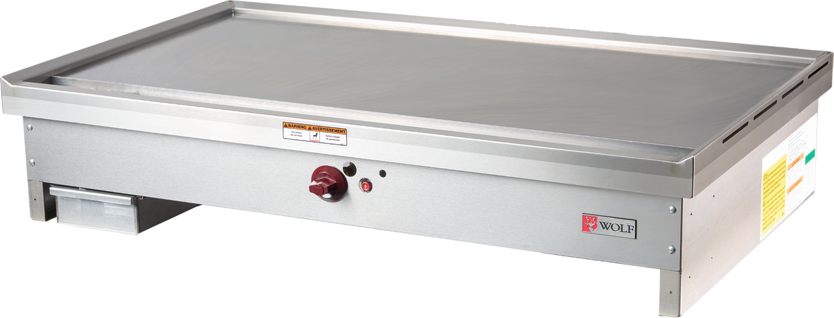 A stainless steel Wolf TYG48C_LP teppanyaki griddle features a flat commercial cooking surface, front control knob, indicator lights, left-side grease tray, and bold Wolf branding in red on the front right corner panel.