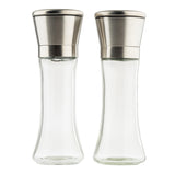 Two empty clear glass salt and pepper mills from TableCraft Products with stainless steel tops stand side by side on a white background. The Salt & Pepper Mill Set features a curved, elegant shape and modern, metallic lids, appearing clean and unused.