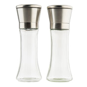 Two empty clear glass salt and pepper mills from TableCraft Products with stainless steel tops stand side by side on a white background. The Salt & Pepper Mill Set features a curved, elegant shape and modern, metallic lids, appearing clean and unused.