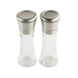 Two clear glass shaker bottles from TableCraft Products, with silver metallic lids, sit side by side on a white background. These glass salt and pepper mills feature a modern, minimalist design with smooth edges and flat-topped lids.
