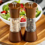 Two wooden salt and pepper grinders with a sleek acacia finish sit side by side on a wooden board. This Salt & Pepper Mill Set is crafted from durable rubberwood, with coarse salt on the left and whole black peppercorns on the right.