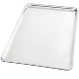 A large, shiny, full size bun sheet pan made from heavy duty aluminum with slightly raised, rounded edges is shown at an angle on a plain white background. The baking sheet has a smooth surface and appears clean and empty.