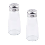 Two clear glass Salt/Pepper Shaker bottles with stainless steel tops sit upright on a white background, side by side with a slight gap. Their silver lids feature small dispensing holes and the shakers are empty.