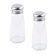 Two clear glass Salt/Pepper Shaker bottles with stainless steel tops sit upright on a white background, side by side with a slight gap. Their silver lids feature small dispensing holes and the shakers are empty.