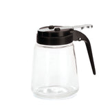 This TableCraft Modern Glass Dispenser features a black plastic lid and handle with a lever for easy pouring. The clear, empty jar is dishwasher safe, and its shape and details are highlighted against the plain white background.