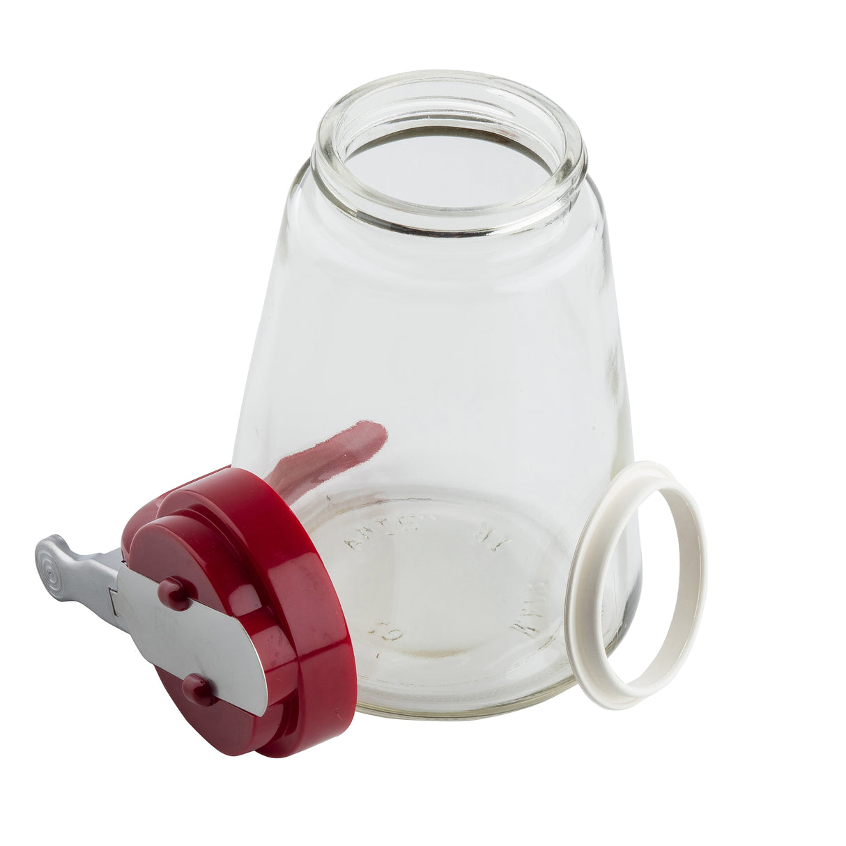 A clear, empty glass dispenser jar is shown with its mouth facing upward. Its red ABS top with a silver locking lever and a separate white rubber ring gasket are placed next to it on a white background. The jar is also dishwasher safe.
