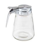 A clear glass dispenser by TableCraft with a chrome plated top and lever is shown on a white background. It features a wide, round base that tapers upward and a hinged, spouted lid designed for easy pouring.