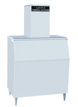 A large, rectangular commercial nugget-style ice maker with angled front door, four metal legs, and a tall box housing labeled "Commercial Ice Machine" on top. The light gray machine stands against a plain, light background.