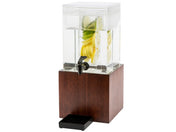 A square BPA free glass beverage dispenser filled with water and slices of lemon, lime, and cucumber sits on a wooden base. It features a black spigot for pouring, a drip tray beneath the spout, and a modern, elegant design.