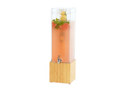 A tall, clear BPA free beverage dispenser with a silver spout and a bamboo base holds pink liquid with watermelon slices, lemon slices, and mint leaves floating at the top. The dispenser is set against a plain white background.