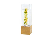 A tall, clear Madera Beverage Dispenser with a silver spigot sits on a wooden base. This 3 gallon infuser holds water with lemon and lime slices stacked vertically inside. The background is plain white.