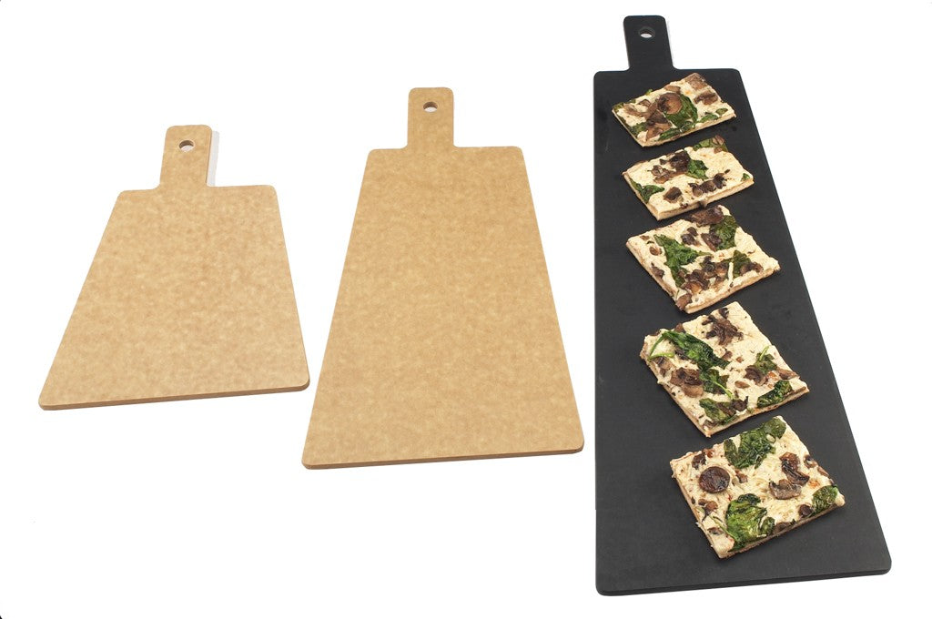Three cutting boards are shown: two plain tan boards on the left and one long black phenolic resin serving/display board on the right. The black board holds five rectangular slices of flatbread topped with spinach and mushrooms; all boards have a handle with a hole.
