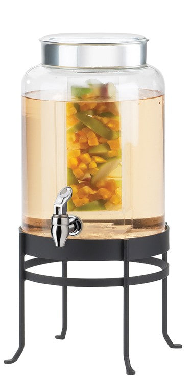 A large BPA free glass beverage dispenser with a metal lid and spigot sits on a black metal stand. The dispenser contains light-colored liquid with chunks of yellow and green fruit, likely infused water.