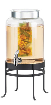A large BPA free glass beverage dispenser with a metal lid and spigot sits on a black metal stand. The dispenser contains light-colored liquid with chunks of yellow and green fruit, likely infused water.