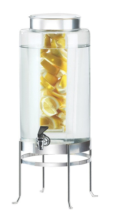 A BPA Free glass beverage dispenser with an infusion chamber holds water and lemon slices. It features a metal lid, a spigot at the bottom, and stands on a tall, silver metal base with four legs.
