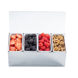 A stainless steel condiment holder with four open sections holds sliced strawberries, blackberries, raspberries, and walnut halves. The box lid is open, each type separated in its own white compartment. The background is plain white.