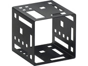 A black metal Squared Cube Riser with geometric cutouts features variously sized square and rectangular openings on all six sides, arranged in a grid-like pattern. The cube sits angled, revealing three faces with uniquely shaped cutouts.