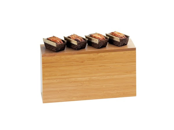 A rectangular Cal-Mil bamboo riser with four small loaves of bread in dark paper liners neatly arranged in a row on top, all against a plain white background.