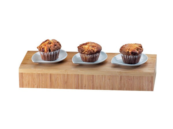 Three golden-brown muffins sit on small white plates, displayed in a row atop a sleek bamboo tray against a plain white background.