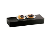 A black rectangular display riser holds two white plates, each with a fruit tart topped with blueberries and thin slices of fruit, arranged side by side, against a plain white background.