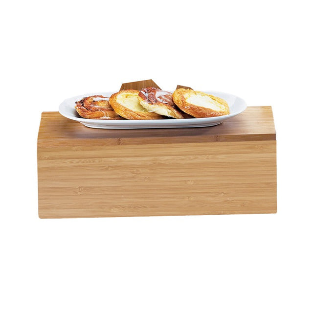 A white oval plate with several pastries sits atop a Cal-Mil bamboo display crate, shown against a plain white background. The pastries appear golden brown with various fillings on top.