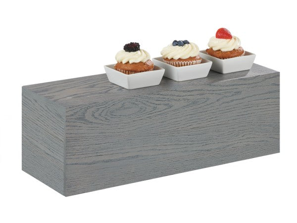 Three cupcakes with white frosting and berries on top are placed in small square white bowls, arranged in a row on an Ashwood Display Riser, showcasing the distinct wood grain texture.