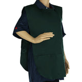 A mannequin dressed in a dark blue collared shirt wears a dark green cobbler apron with two front pockets. Made from a poly-cotton blend, the machine washable apron ties at the back, covering the torso. The left hand rests on its hip; the right arm hangs down.