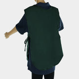 A mannequin displays a dark green cobbler apron, crafted from a durable poly-cotton blend and tied at the sides. The apron covers the upper body to the thighs over a dark shirt. The mannequin’s right arm is bent outward against a white background.