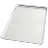 A full size, heavy weight aluminum sheet pan with a raised edge on all sides sits empty on a white background. Its smooth, shiny surface is clearly visible, and the tray is photographed at an angle.