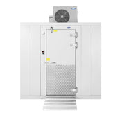 A large commercial walk-in freezer with a white, insulated exterior, metal diamond-plate kick plate on the door, silver hinges, and a top-mount refrigeration system. A small control panel and a metal ramp are positioned in front of the door.