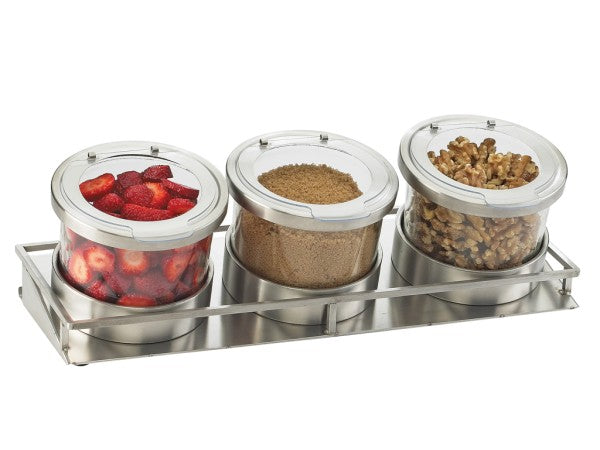 Three stainless steel canisters with clear lids are arranged in a cold condiment display tray. The left canister contains sliced strawberries, the middle holds brown sugar, and the right is filled with walnut halves—all visible through the transparent lids.