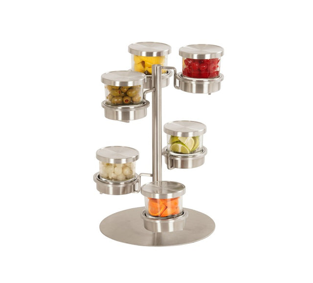 A stainless steel stand showcases six round glass jars, each filled with garnishes—orange slices, red cherries, green olives, lemon slices, white onions, and carrot sticks—arranged on a tiered Mixology jar display that rotates for easy access.