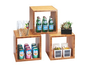 Three wooden Cal-Mil bamboo cube shelves display glass bottles of sparkling water, tall glasses with a cocktail, cans of flavored water, two containers labeled limes and lemons, and a small potted succulent in an organized library cube riser setup.