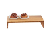 A Cal-Mil bamboo step riser holds two white square plates, each topped with a sticky pecan pastry. The setup is on a plain white background, emphasizing the wood texture and neatly presented desserts.