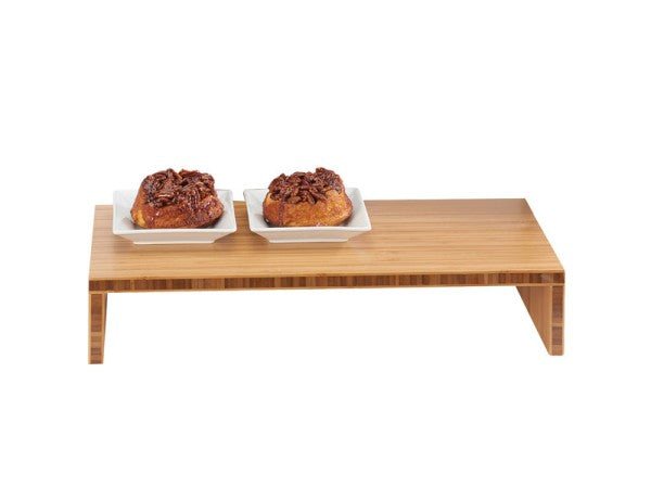 A Cal-Mil bamboo step riser holds two white square plates, each topped with a sticky pecan pastry. The setup is on a plain white background, emphasizing the wood texture and neatly presented desserts.