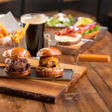 Two mini burgers on a wooden tray—one with cheddar cheese and fried onions, the other with red onions and sauce—served alongside a pint of dark beer and fries. Perfect for serving with the Slider Flight Spatula, which is stainless steel and dishwasher safe.