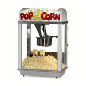 A classic Unimaxx kettle popcorn machine with glass sides, filled with a large mound of popcorn. Two striped containers rest among the popcorn. The top marquee reads POP CORN in bold red letters with popcorn graphics on a white background.