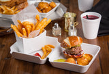 A white melamine box holds a Better Burger Collection favorite—a burger with lettuce, tomato, and red onion on a pretzel bun—served with pickles, fried cheese balls, and curly fries. The tray is dishwasher safe for easy cleanup on the rustic wooden table.