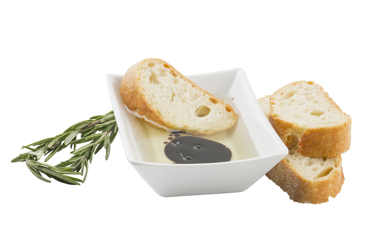 A white melamine square bowl holds olive oil and balsamic vinegar, with a slice of crusty bread soaking in the mixture. Two more bread slices and a sprig of fresh rosemary rest beside the bowl, all set against a white background.