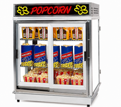 A large silver popcorn shelf warmer with a glass front displays bags and boxes of popcorn. The top has a red neon POPCORN sign with yellow popcorn illustrations, while the corn freshener system keeps the ready-to-serve popcorn fresh on the shelves.