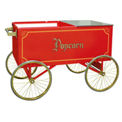 A vintage-style red popcorn wagon with gold trim, four large spoked wheels, and “Popcorn” in ornate gold lettering on the side. The sturdy Gold Medal Products cart features a stainless steel counter top and a flat metal surface for easy serving.