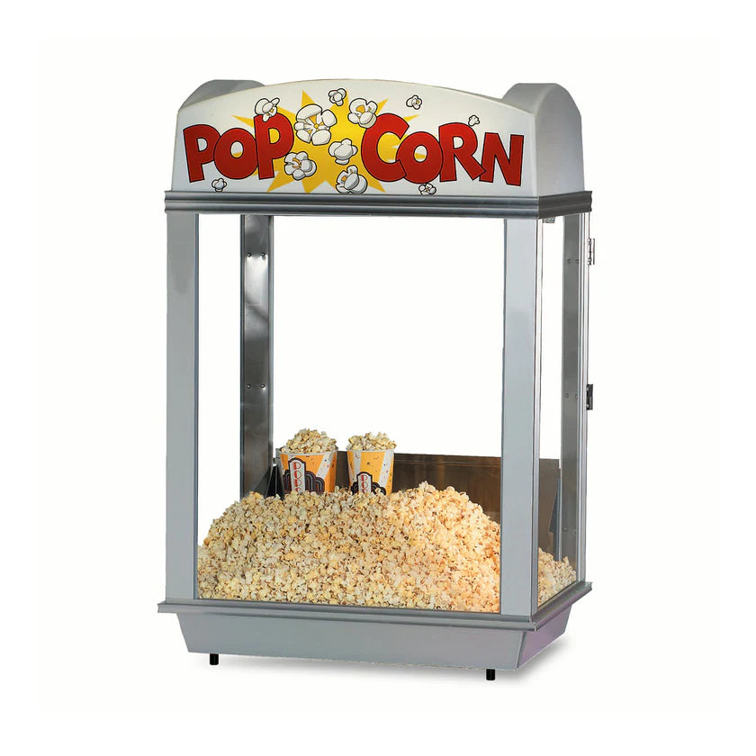 A metal and glass Gold Medal Products popcorn machine filled with a large heap of popcorn, two cartons sticking out of it. The top sign reads POPCORN in red letters with illustrated kernels. The background is plain white.
