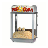 A metal and glass Gold Medal Products popcorn machine filled with a large heap of popcorn, two cartons sticking out of it. The top sign reads POPCORN in red letters with illustrated kernels. The background is plain white.